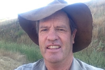 A farmer, wearing a hat, stands in a paddock