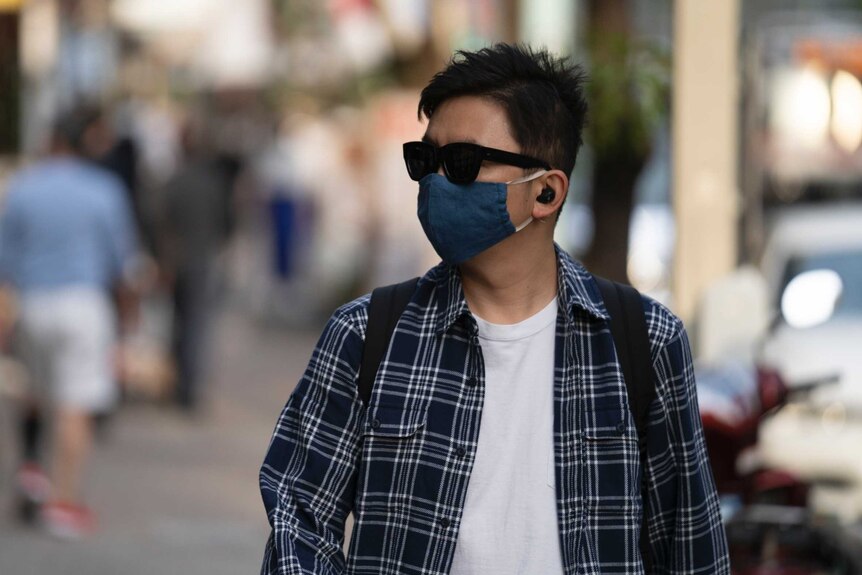 A young Japanese man walking down a street in a face mask