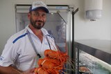Seafood shop manager, in overalls, holding a tray of Western Rock Lobster or crayfish.