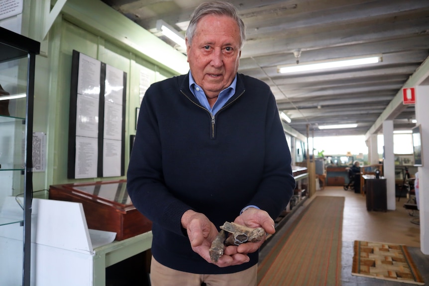 A man in a navy blue jumper holds out fossilised bones in his hands.