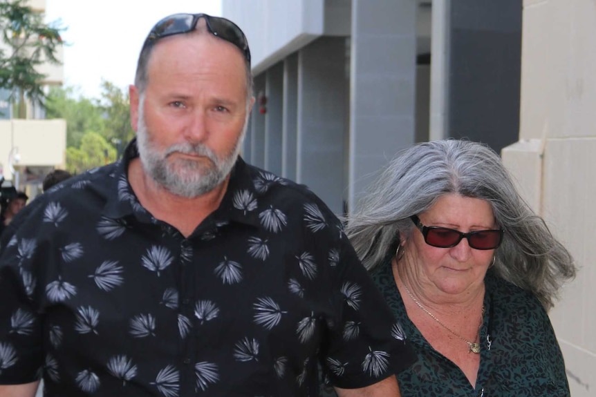 A man and woman hold hands as they walk on the street outside court.