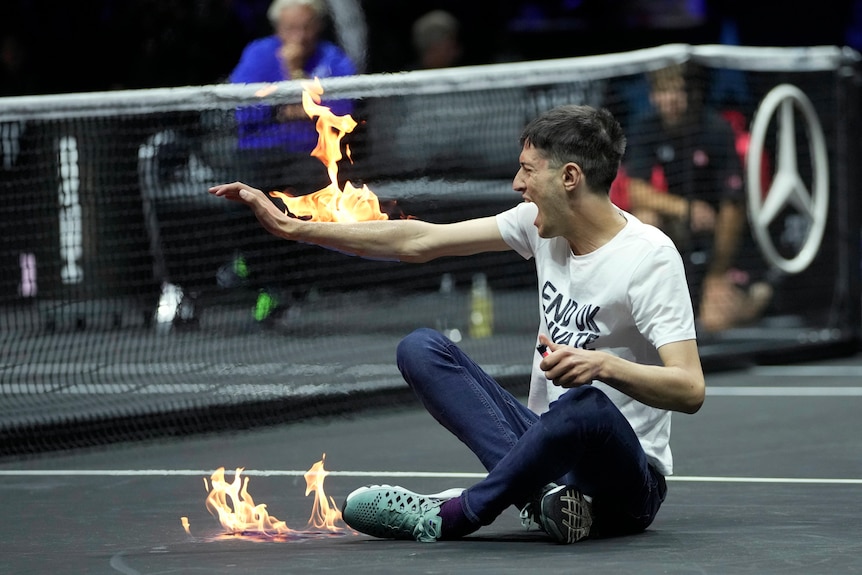 A man's arm is on fire while he sits on a tennis court. 