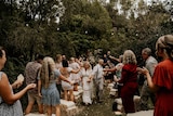 A bride and groom are showered with confetti at an outdoor wedding.