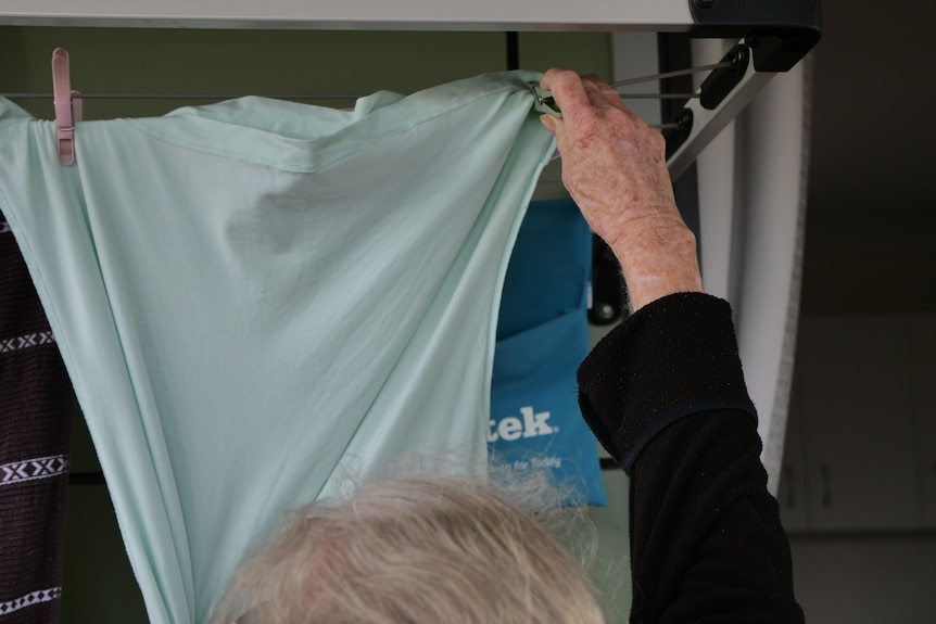 An older woman's hand placing a peg on a green shirt on a clothes line. 