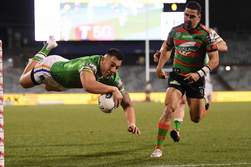 Nick Cotric is horizontal as he dives towards the try line with the ball in one hand. A Souths opponent trails behind him