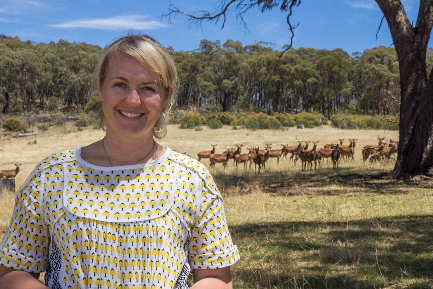 A woman in the foreground in a paddock with deer in the background