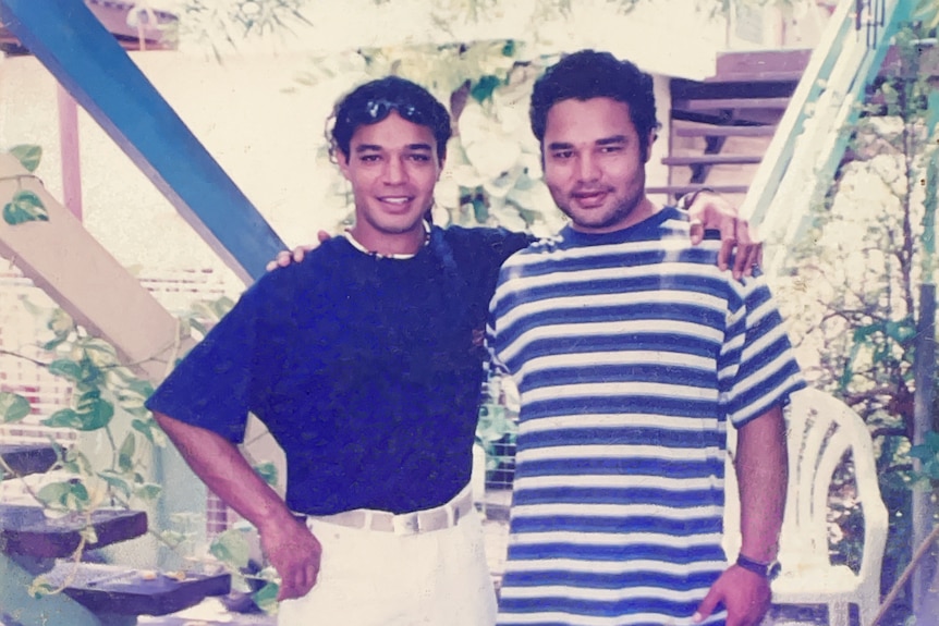 Two Indigenous men in blue shirts standing with an arm around each other.