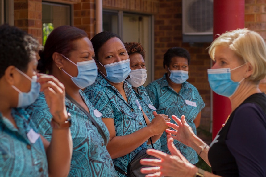 Aged care workers in uniform and wearing masks speak to their boss.