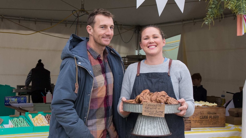 A man and woman standing in front of a stall selling cakes and biscuits