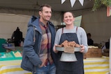 A man and woman standing in front of a stall selling cakes and biscuits