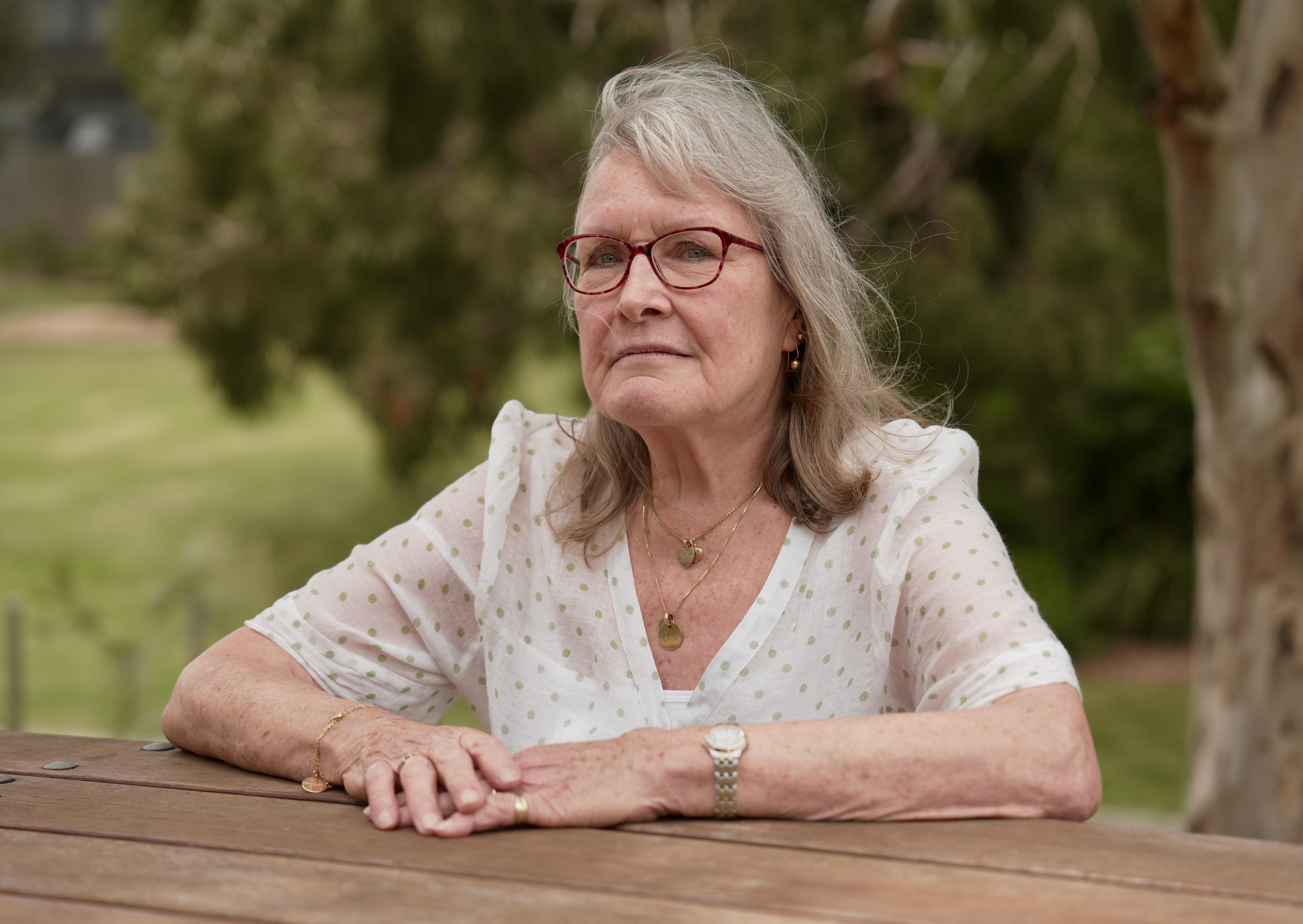 Hennie van Leeuwen está sentado en una mesa de picnic al aire libre y tiene una expresión seria en su rostro.