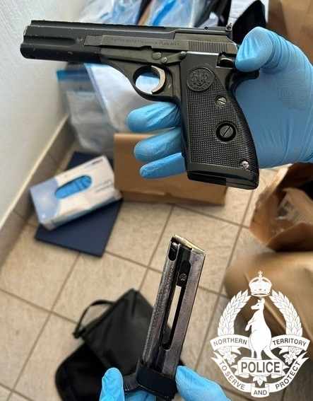 A person wearing latex gloves holds a black pistol.