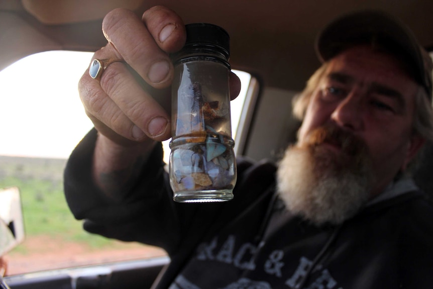 man with inside a truck holding a glass container full of opal fragments