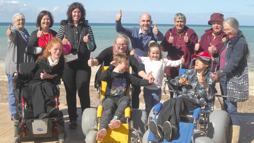 Group of happy people at the beach, three in wheelchairs, people holding thumbs up