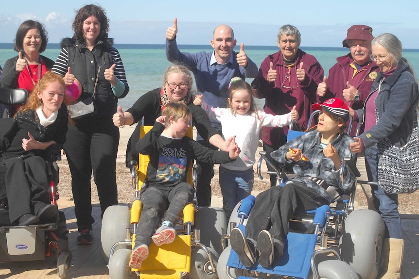 Group of happy people at the beach, three in wheelchairs, people holding thumbs up