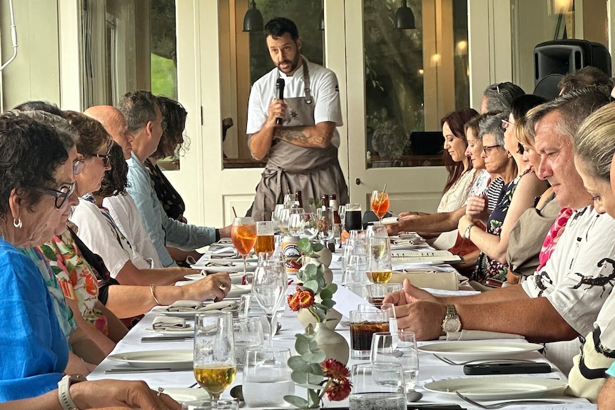 A chef addresses a table full of people.