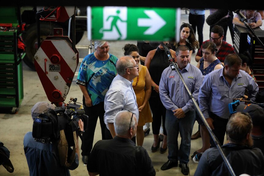 Mr Morrison stands below an exit sign while speaking with workers in a factory