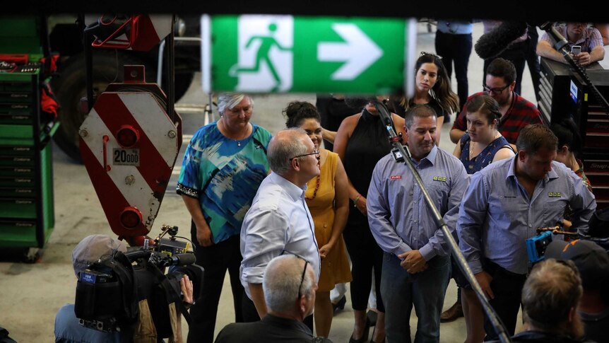 Mr Morrison stands below an exit sign while speaking with workers in a factory