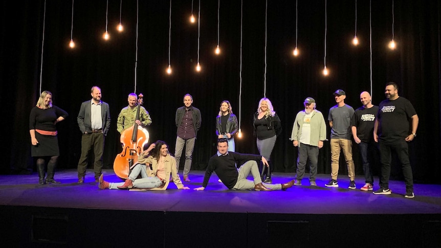 12 people standing on stage, one holding a cello