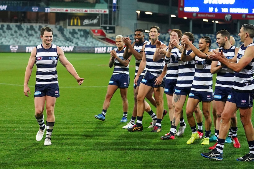 An AFL player smiles as he walks off the ground past a row of his cheering teammates.