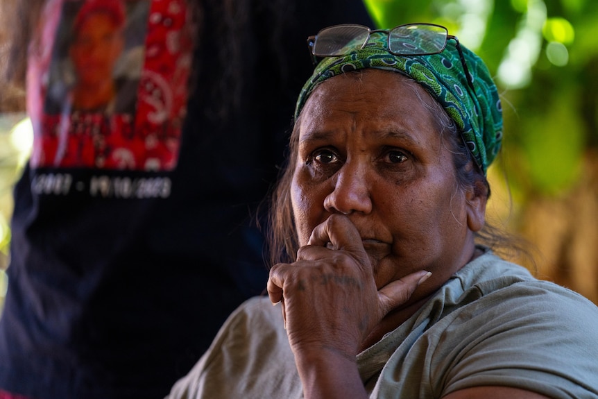 An Indigenous woman with a green head band looks distraught
