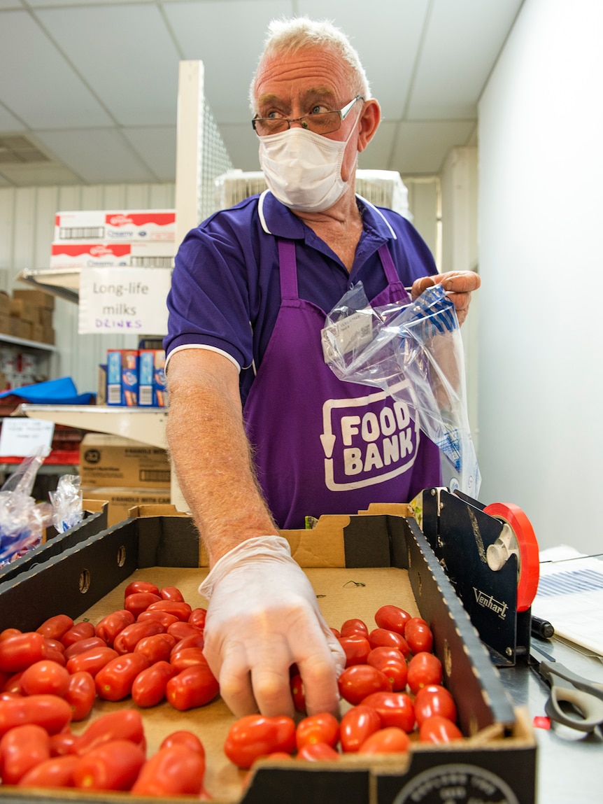 a man in a purple foodbank outfit packs a bag with tomatoes