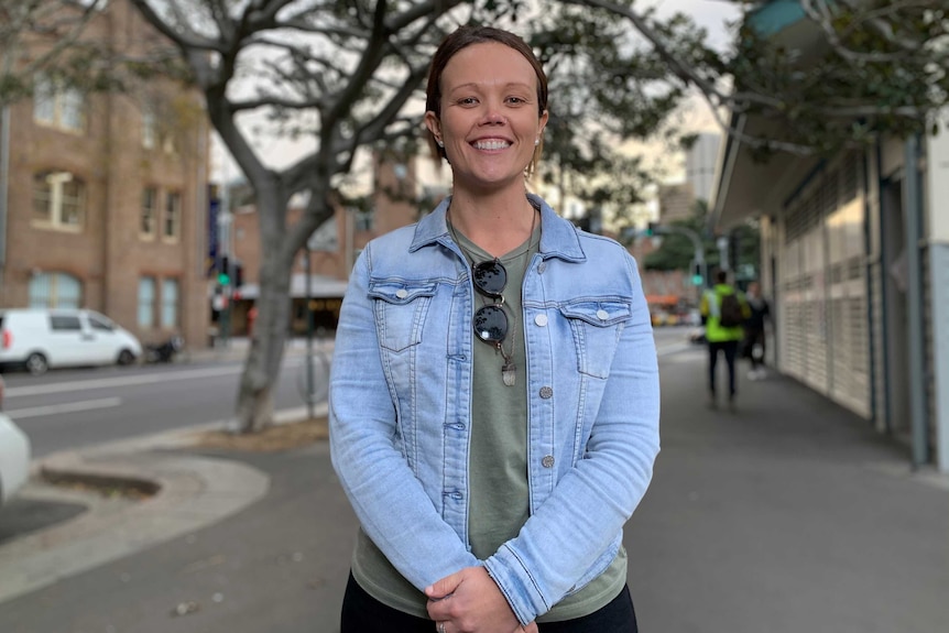 A woman in a denim jacket stands on a footpath.