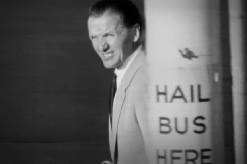 Old black and white photograph of a man squinting at the streetscape around him.