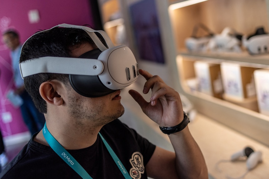 A close up of a man wearing a virtual reality headset over his eyes, with straps over his head. He touches device with his hands