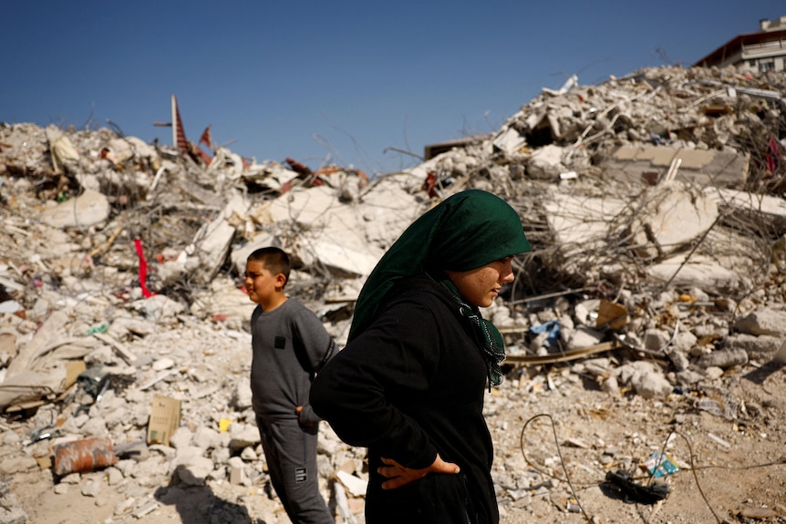 A girl and a boy stand among rubble. 