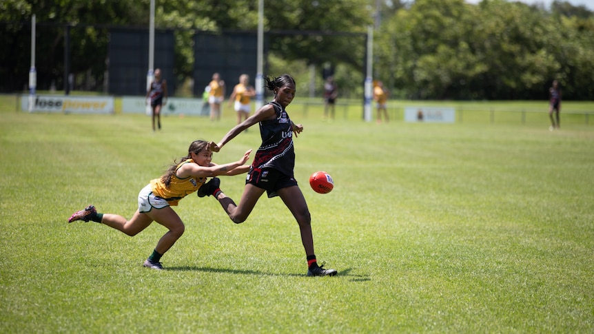 A woman playing Australian Rules football is about to be tackled