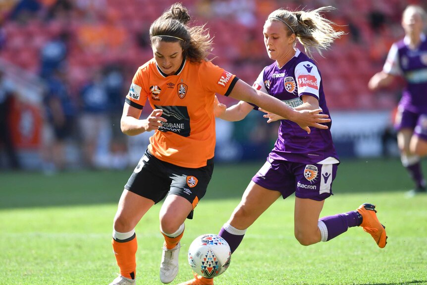 Jenna McCormick in orange on the left, runs past Rachel Hill in purple with a soccer ball at her feet