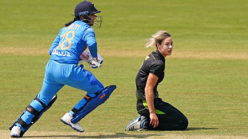 Ellyse Perry sits on her knees on the ground as Smriti Mandhana sets off on a run