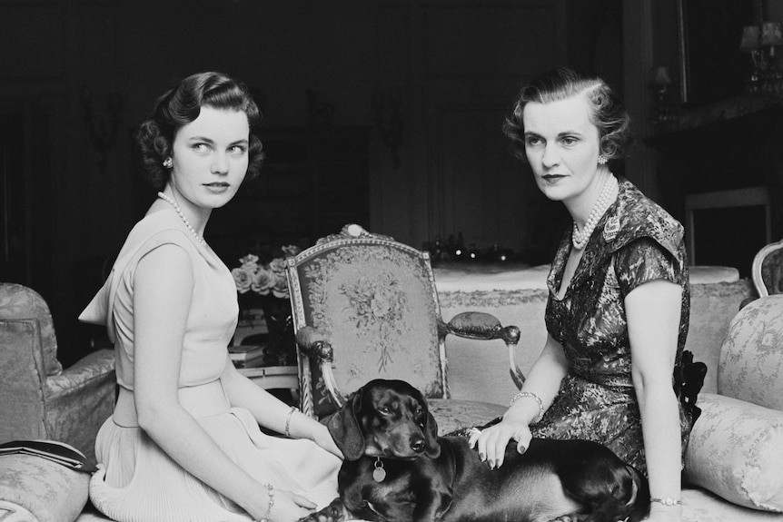 A black and white photograph of Margaret in an elegant blouse with a sting of pearls around her neck sitting with a young woman