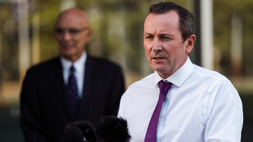 Man in suit speaks behind podium with microphones