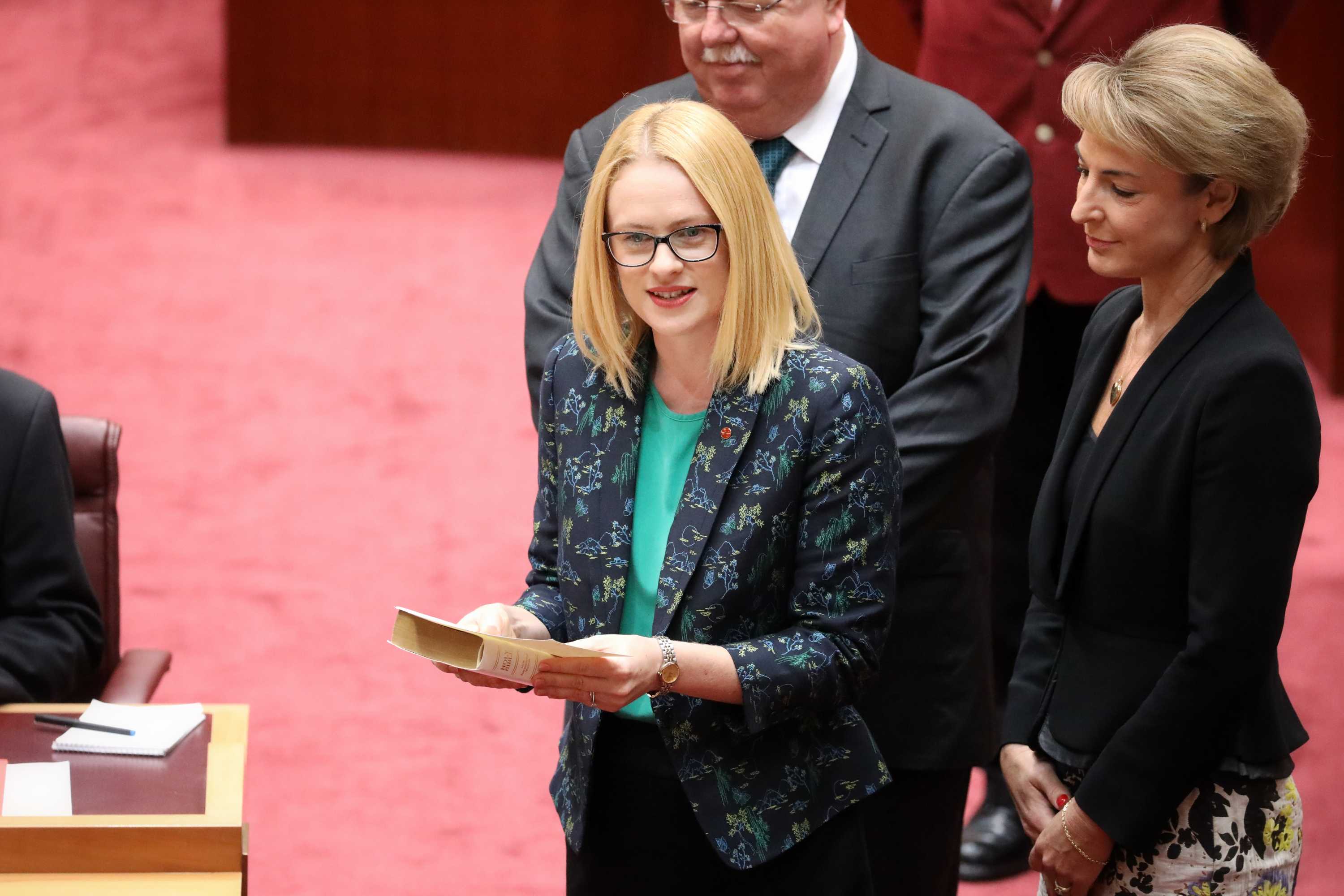 Stoker is on the floor of the Senate holding a bible, flanked by Michaelia Cash and Barry O'Sullivan.