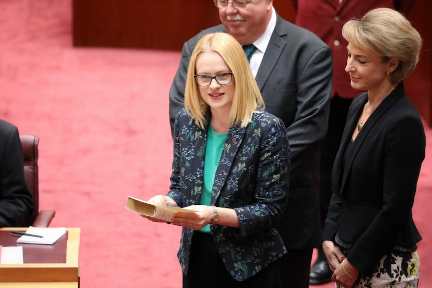 Stoker is on the floor of the Senate holding a bible, flanked by Michaelia Cash and Barry O'Sullivan.