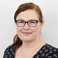 Karen Stace wearing glasses and smiling at the camera in front of a plain white background.