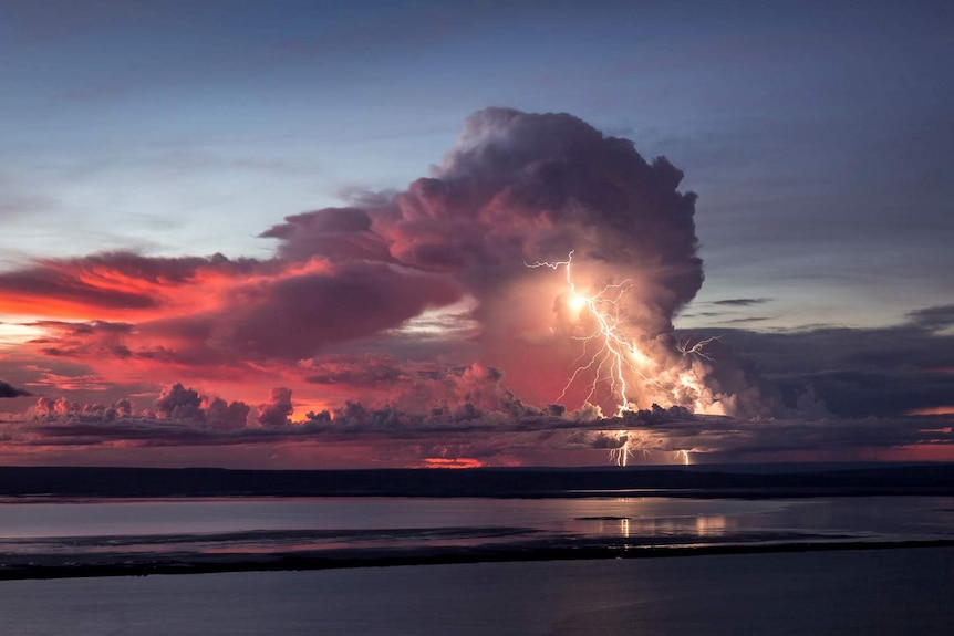 Pink and grey clouds and a huge lightning bolt on the horizon over hills and water near Wyndham.