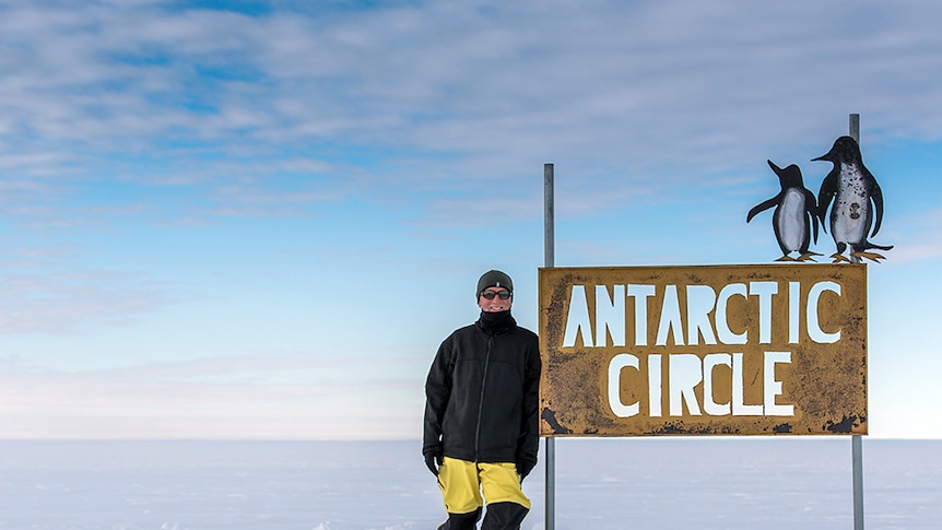 Nick Gales stands next to a sign in Antarctica