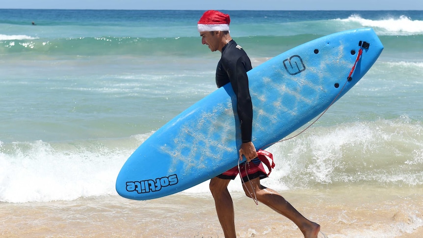 A surfer leaves the water wearing a Santa Claus Hat on Christmas Day