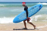 A surfer leaves the water wearing a Santa Claus Hat on Christmas Day