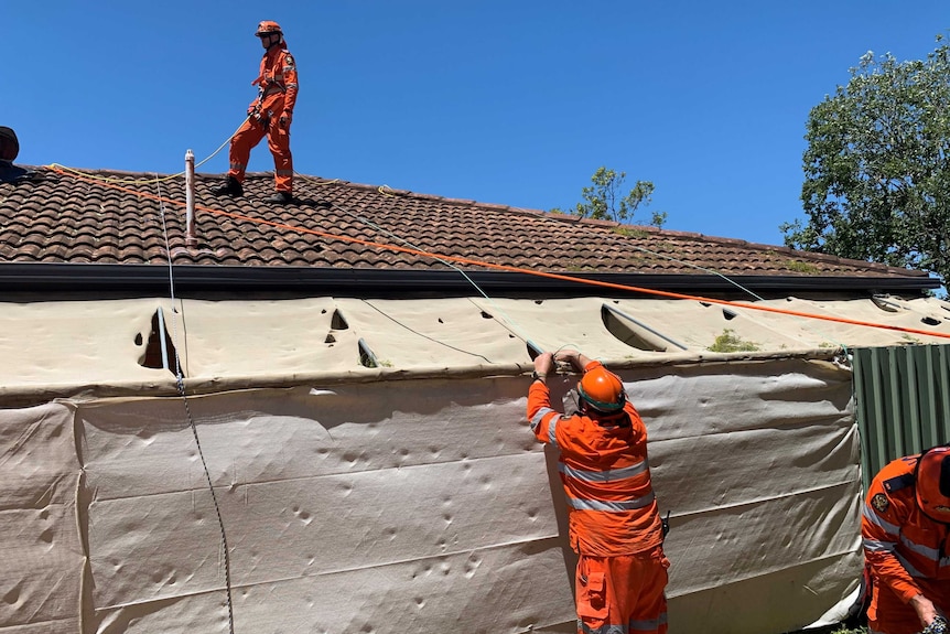 SES volunteers cover holes in the roof of a home at Rosewood after wild hailstorms.