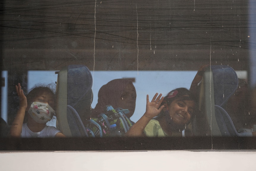 Children wave bye from a bus