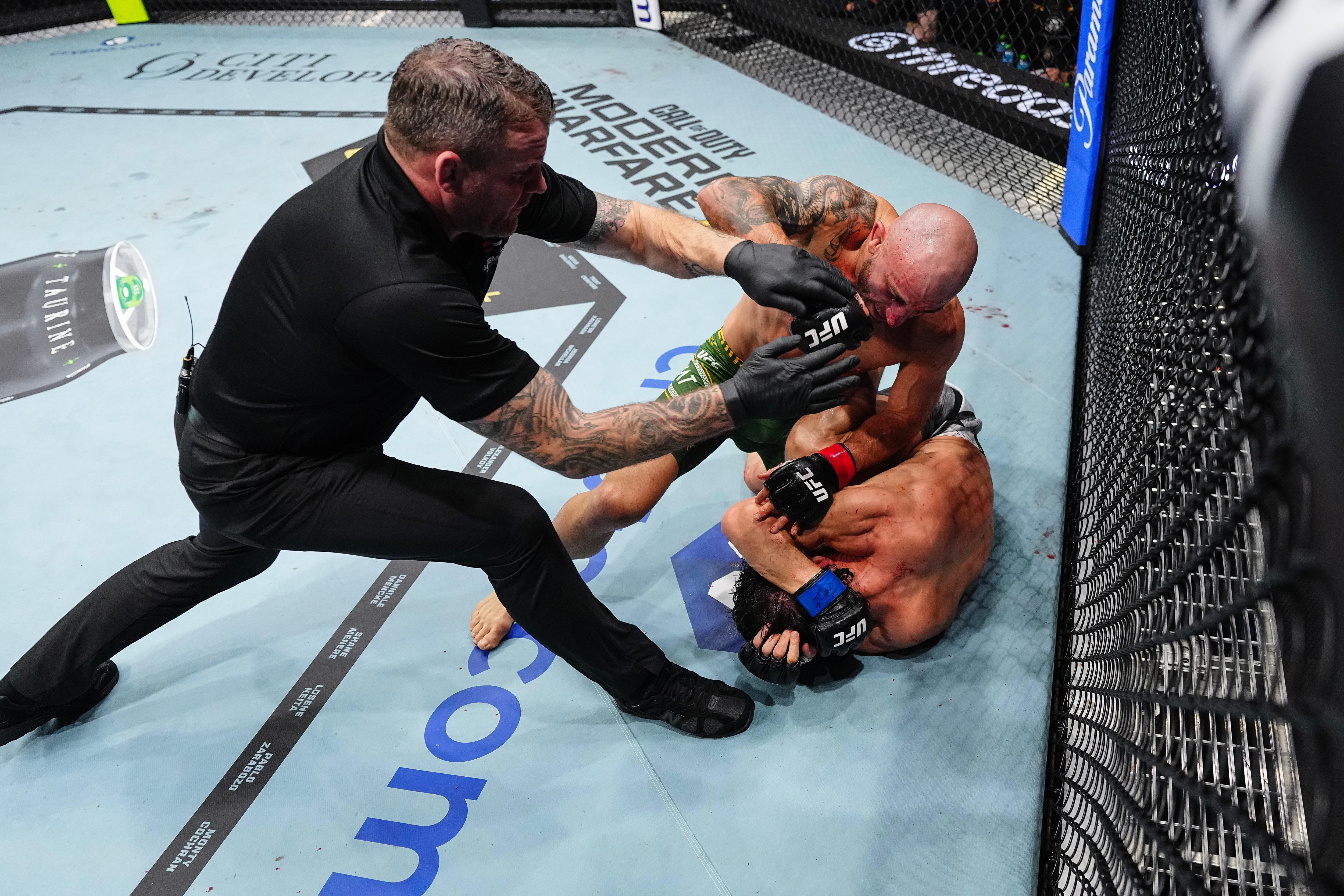 A referee steps in to separate two UFC fighters as one man punches down on a man protecting himself.