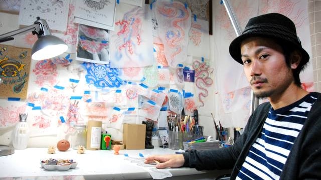 Tattoo artist Taiki Masuda sitting at a desk in his Osaka studio, surrounded by sketches and artwork.