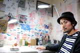 Tattoo artist Taiki Masuda sitting at a desk in his Osaka studio, surrounded by sketches and artwork.
