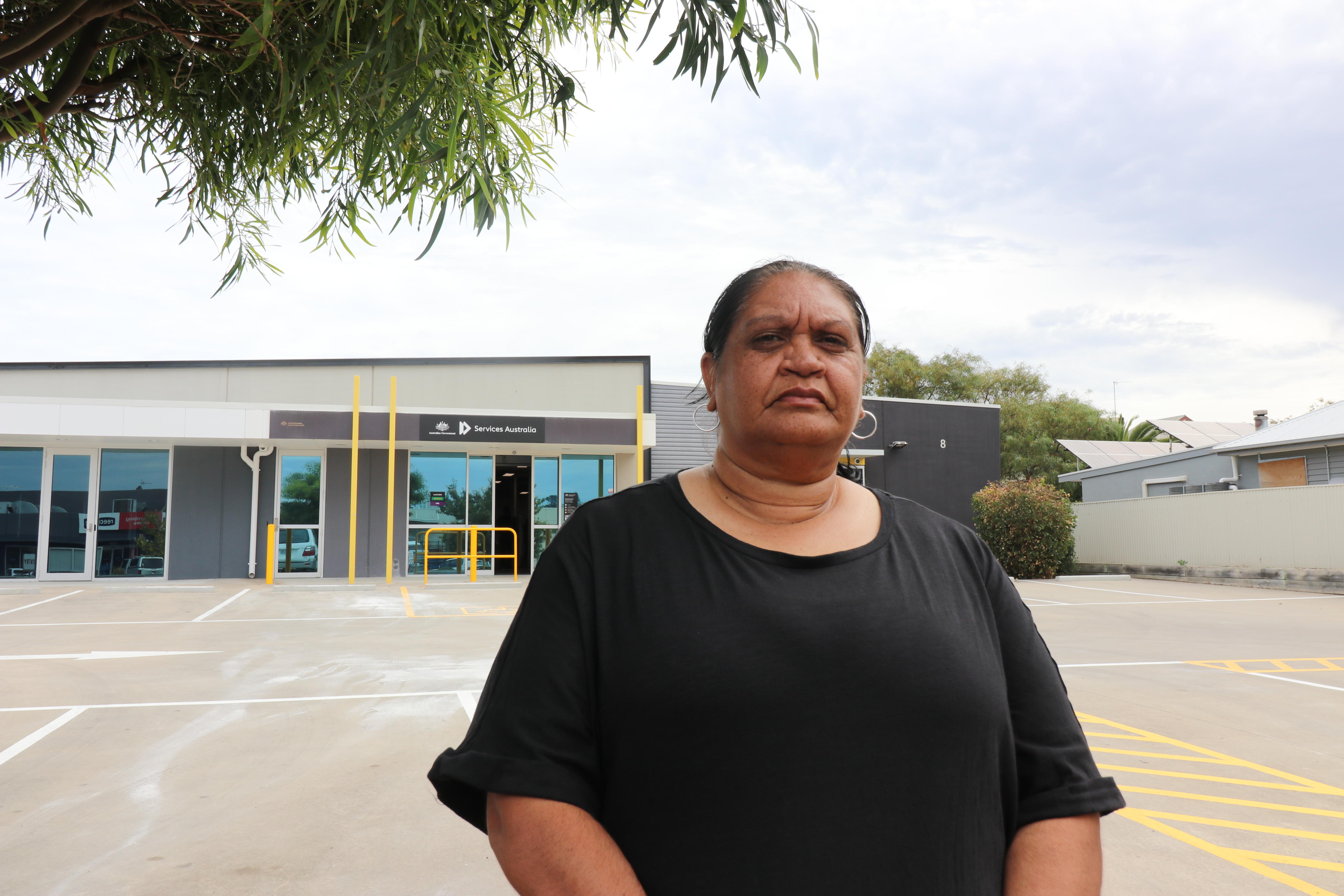 Emma Richards wears a black tshirt and stands in front of a services australia building with a carpark.