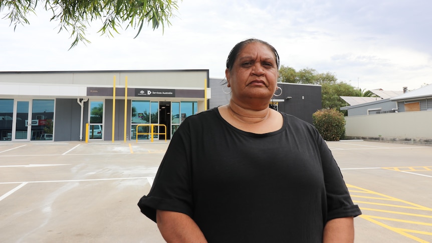 Emma Richards wears a black tshirt and stands in front of a services australia building with a carpark.