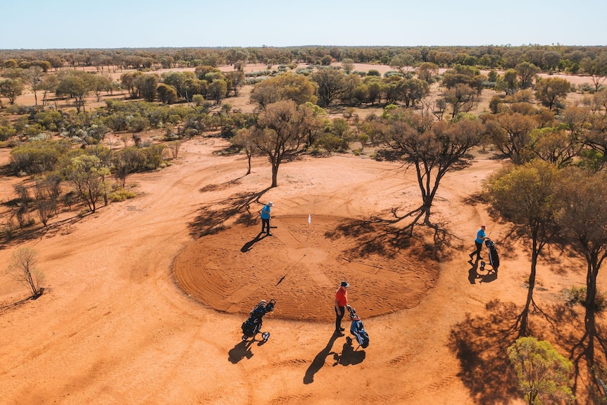An aerial shot of people playing golf on a red dirt outback course.